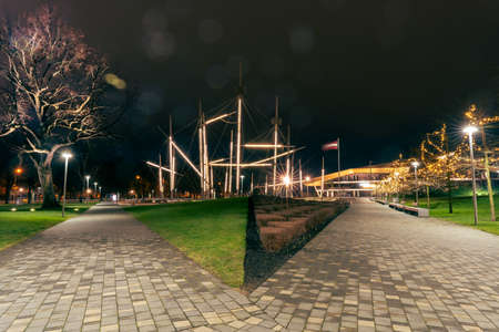 Autumn view in Ventspils park with a green grass and neatly pruned bushes without leaves in the background you can see a fountain, trees and a concert hall.の写真素材