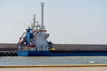 Estonia, a cargo ship in blue and white is moored at Virsti berth.The cargo ship is moored at the port berth where a person serves the ship's hatches, creating an idea of the ship's size and scale.の写真素材