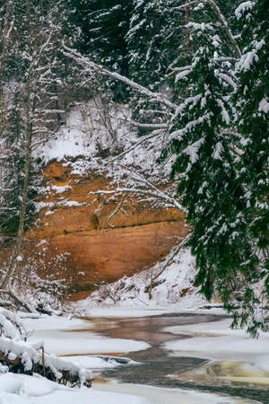 The Rauna River is frozen and covered with snow, and the RaibÄs cliffs can be seen in the distance. In the middle of the river we see a narrow strip of water, which has broken out of the ice freeze.の写真素材
