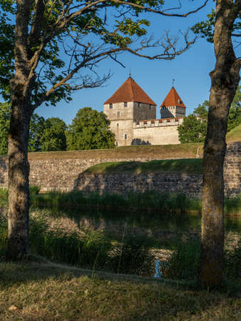 Estonia, Saaremaa Island. A beak to the tower of Kuressaare Castle opened through the trees.View across the canal to the medieval castle fortifications and castle towers in the evening sunのeditorial素材