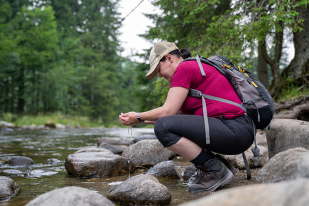 a woman on a hike stops by a stream and draws water summer timeの写真素材