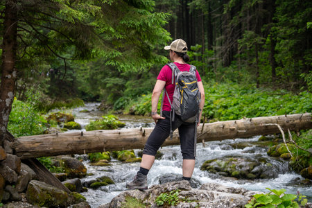 a woman on a mountain hike stops by a stream and looks where to go next in summerの写真素材