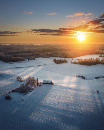 Aerial view of beautiful sunrise above snowy field with an old barn with long shadows.の写真素材