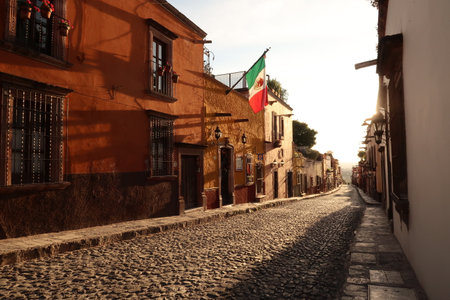 Typical cobblestone street in San Miguel de Allende at golden hour/sunset, a Mexican flag is hanging on a facade, Mexico 2022の写真素材