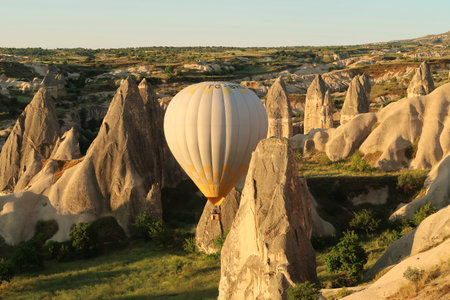 Yellow and white hot air balloon maneuvering between the fairy chimneys of Cappadocia, close to Gの写真素材