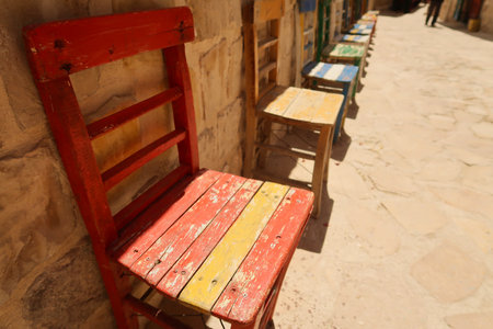 A row of colorful wooden chairs in a row in front of a wall in the old town of Mardin, Turkey 2022の写真素材