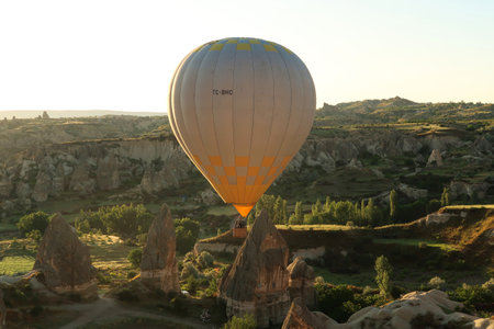 Yellow and white hot air balloon illuminated by the early morning sun while flying over the landscape of Cappadocia with its famous fairy chimneys, close to Gの写真素材