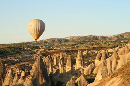 Yellow and white hot air balloon flying over the landscape of Cappadocia with its famous fairy chimneys, close to Gの写真素材