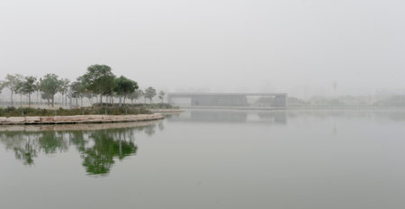 Urban landscape of Beersheba, Israel, featuring modern residential buildings, a green city park, trees, water reflection, and contemporary architecture on a foggy morning.の写真素材
