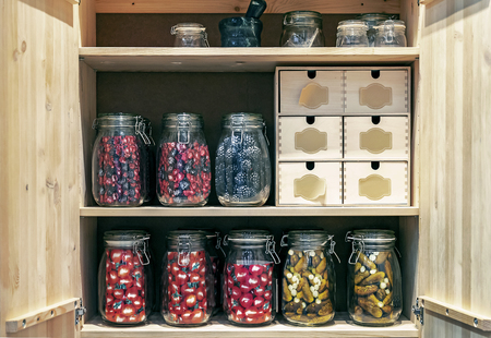 Wooden cabinet with glass jars of pickles and marinades in a conceptual style.