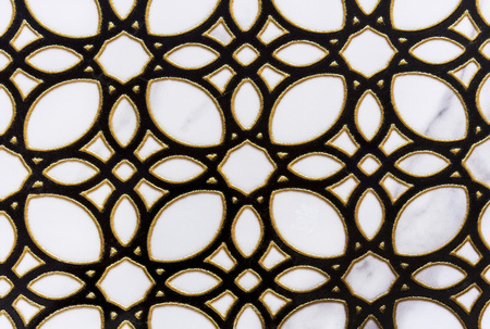 Black openwork ornament with a gold border on a white ceramic tile.の写真素材