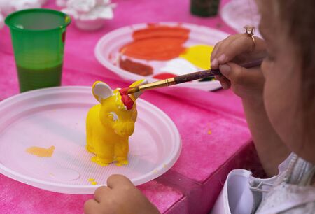 Child paints a ceramic figurine with bright colors. Ceramic staruette for coloring.の写真素材