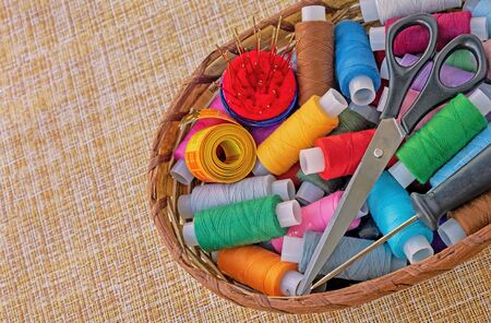 Multicolored sewing threads in a wicker basket. Spools of thread for sewing. The concept of sewing accessories.の写真素材