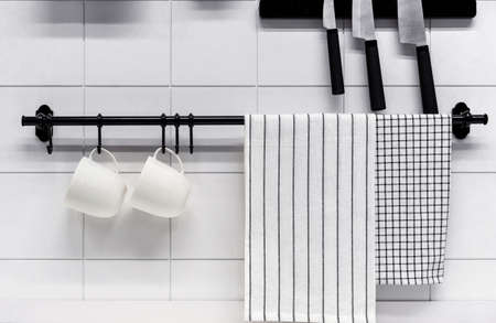 Two white mugs and two towels on a black kitchen rail.