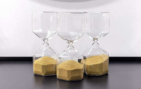 Glass hourglass with yellow sand on a dark wooden table.