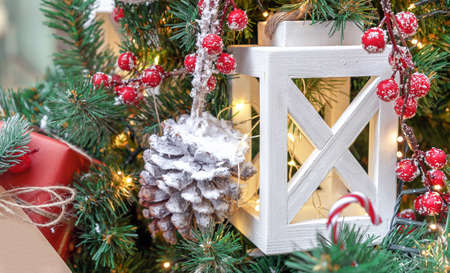 White wooden lantern with a garland, a snowy pine cone and red berries on a Christmas tree.の写真素材