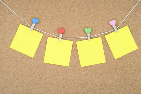 Four yellow stickers on a rope with multi-colored clothespins. Stickers on the cork board.の写真素材