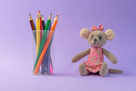 Colored pencils in a plastic cup and a toy mouse on a lilac background.の写真素材
