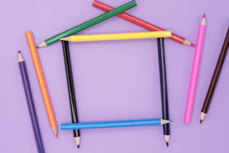 Colored pencils for drawing in the shape of a house on a lilac background.の写真素材