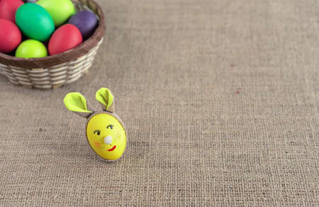 Yellow egg in the shape of an Easter bunny and multicolored eggs in a wicker basket.の写真素材