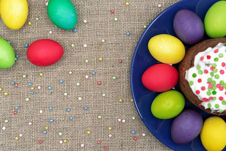 Round plate with multicolored Easter eggs and Easter cake on a burlap background.の写真素材
