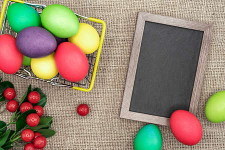 Multicolored Easter eggs in a metal basket and a frame with a chalk board.の写真素材