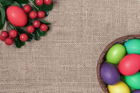 Multicolored Easter eggs in a wicker basket and red berries on a burlap background.の写真素材