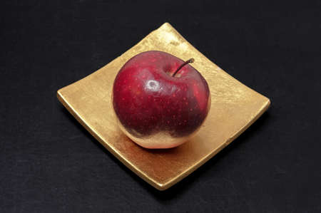 Red apple in a golden square dish on a black background.の写真素材