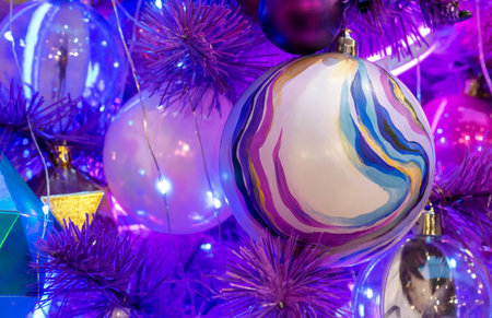 Christmas ball with multicolored stripes on the Christmas tree with magenta-blue backlight.の写真素材