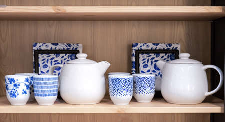 Ceramic teapots and cups with blue ornaments on a wooden kitchen shelf.の写真素材