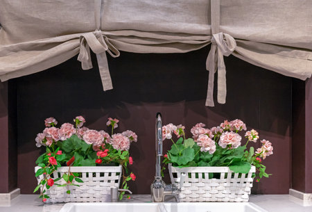 Linen curtain and a planter with pink flowers over the kitchen sink.の写真素材