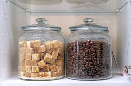 Glass jars with coffee beans and cane sugar on a kitchen cabinet shelf.の写真素材