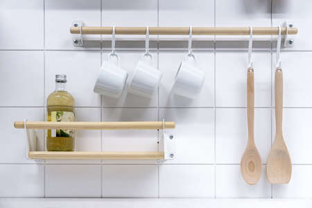 White cups on hooks, wooden spoons and shelf with drink. kitchenware.の写真素材