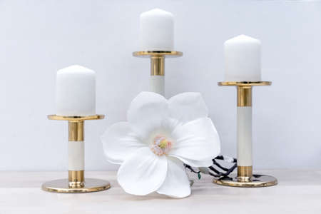 Three white candles on brass candlesticks and a white tropical flower.の写真素材