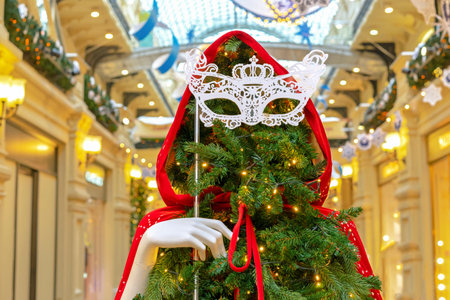 Christmas tree in a red cloak with a hood and an openwork masquerade mask in her hand.の写真素材