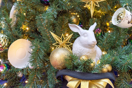 Figurine of a white rabbit near a decorated Christmas tree. Bunny is the symbol of the year according to the eastern calendar.の写真素材