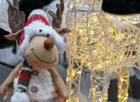 Soft toy of a smiling reindeer in a knitted hat and scarf on the background of Christmas lights.の写真素材