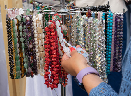 Collection of colorful gemstone necklaces and bracelets on jewelry rack, close-up of woman's hand choosing crystal accessory at marketの写真素材