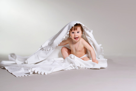 An adorable, laughing baby looking at camera under a white blanket, shot in the studioの写真素材