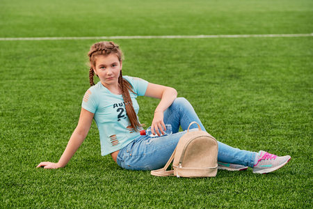A young bright girl loves sports.teenager girl sitting on the school fieldの写真素材