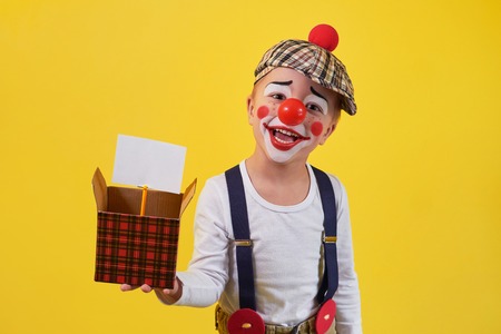 Funny kid clown isolated on yellow background. Beautiful playful portrait child boy jester in makeup. Expression face joy, smile, fun, cheerful. 1 April Fools day concept.の写真素材
