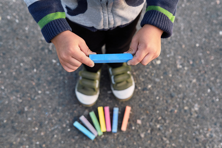 Babys hands holding colorful blue chalk closeup. Childrens Creativity. Early child development,top view.The boys legs, sneakers, asphalt, multicolored chalks, soft focus.の写真素材