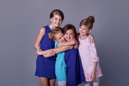 Group happy smiling young teen girls hugging. Friendly embrace of happy,cheerful children. Stylish elegant four children posing at studio in beautiful blue dresses for catalog childrens clothes.の写真素材