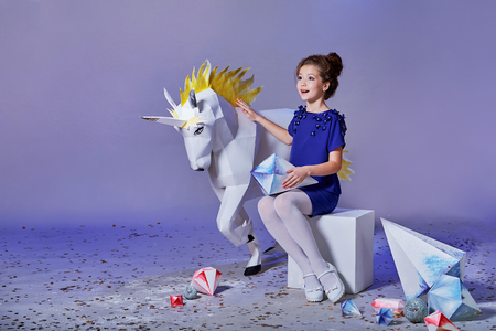 Beautiful little lady girl,fabulous unicorn near.Child elegant blue dress.Looks delight,admiration side,anticipation holiday.Fashion kid,advertising magazine,shop,purple,lilac background,copy space.の写真素材