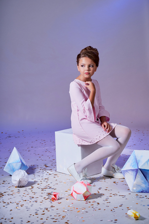 Romantic little girl in beautiful pink dress for teenager sitting,looking away,posing in studio,purple pastel background. Fashion pretty lady child,feminine elegant style.Designer clothes, collection.の写真素材