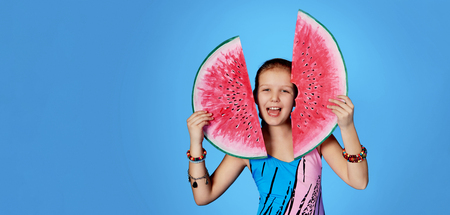 Funny girl in swimsuit holding slice watermelon.Isolated blue background,studio,,copy space for text,design,shop,advertising.Beautiful portrait cheerful,smiles,expression,enjoy.Concept summer.の写真素材