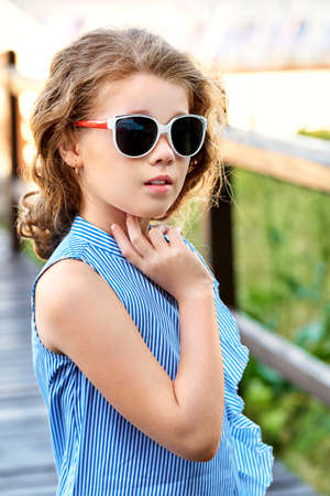 Elegant child portrait. Little girl model wearing summer cool clothing, sunglasses. Marine style, outdoors. Looking away. Fashion kid concept.の写真素材