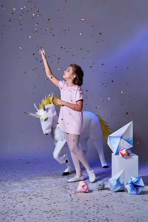 Holidays, christmas, new year, x-mas,concept. Little girl in elegance dress for party pointing finger on glitter confetti. Fashion lady teenage poses full-length in studio, gray purple background.の写真素材