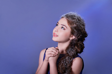 Winter beautiful girl looks copy space for text,advertising. Concept fashion,holiday,new year,christmas. Portrait Asian child, teenager, make-up, on snow hair, studio, isolated purple background.の写真素材