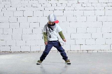 Child model posing in young rapper clothes. Cool kid boy dancing break dance.Hip-hop style. studio, brick wall background.の写真素材